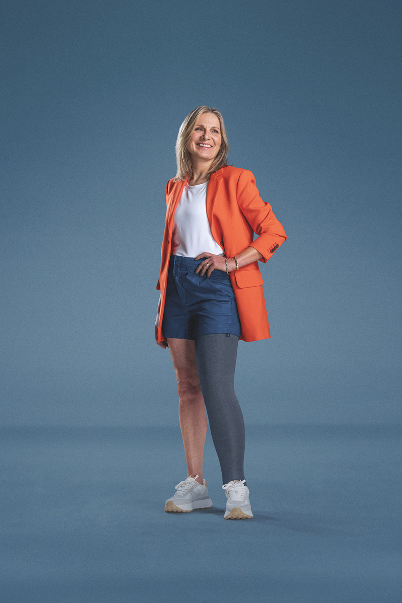 Woman wearing an orange blazer, with one leg in a JOBST Confidence compression garment Woman wearing an orange blazer, with one leg in a JOBST Confidence compression garment